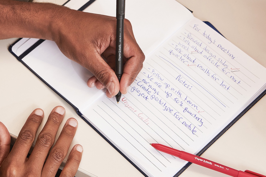 Someone writing in a notebook with a black pen.