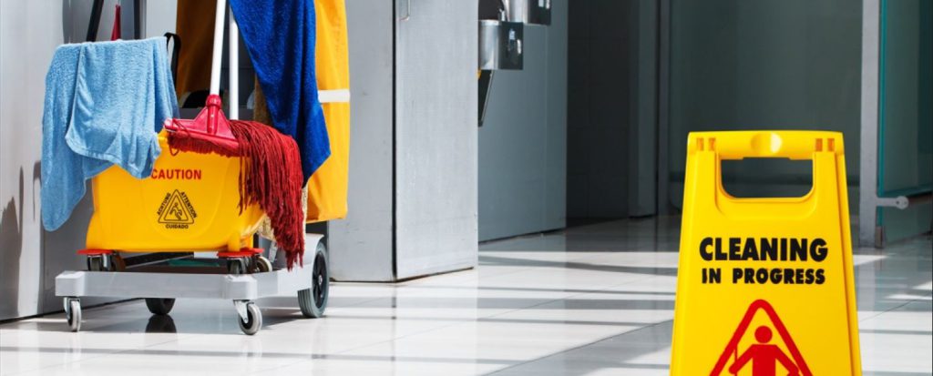 Cleaning cart of janitorial supplies behind cleaning sign