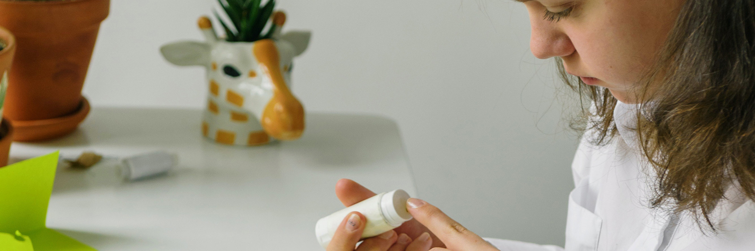 a curious young girl holding a glue stick and touching it with her finger