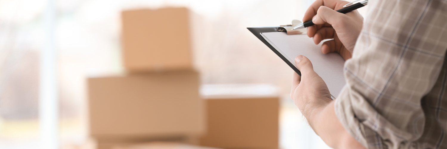 man holding a clipboard checking things off with boxes in the background stacked neatly