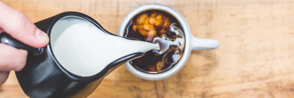 someone pouring milk into a cup full of coffee