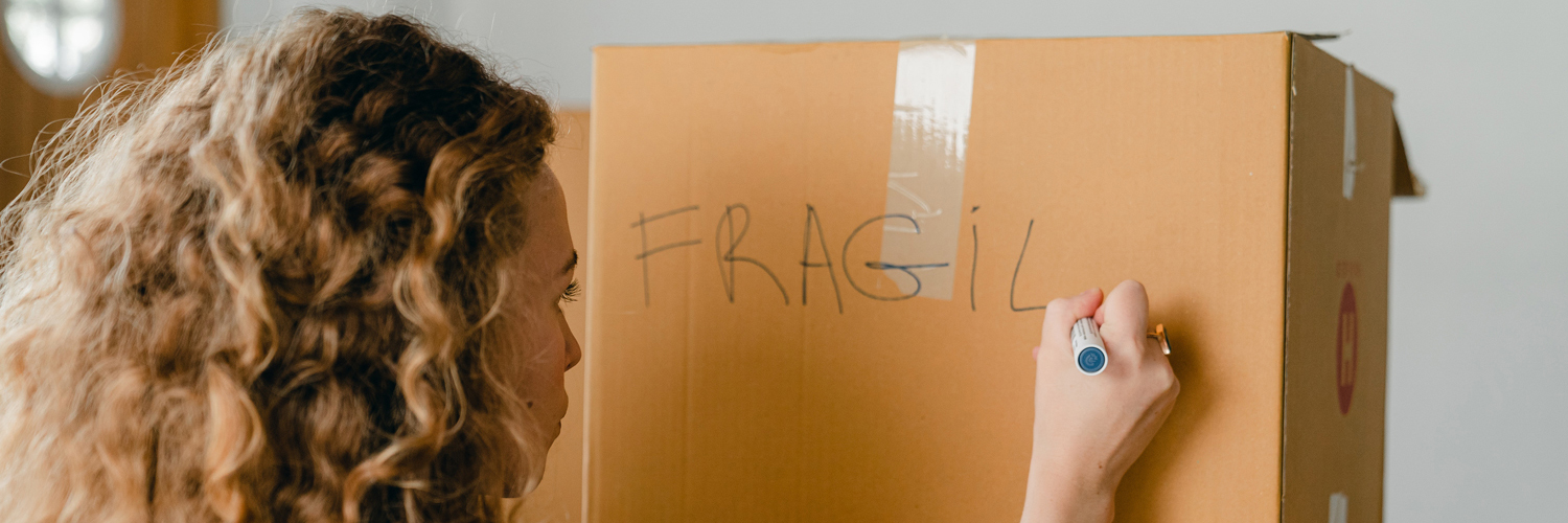 woman labeling her moving box as fragile to indicate fragile items inside the box