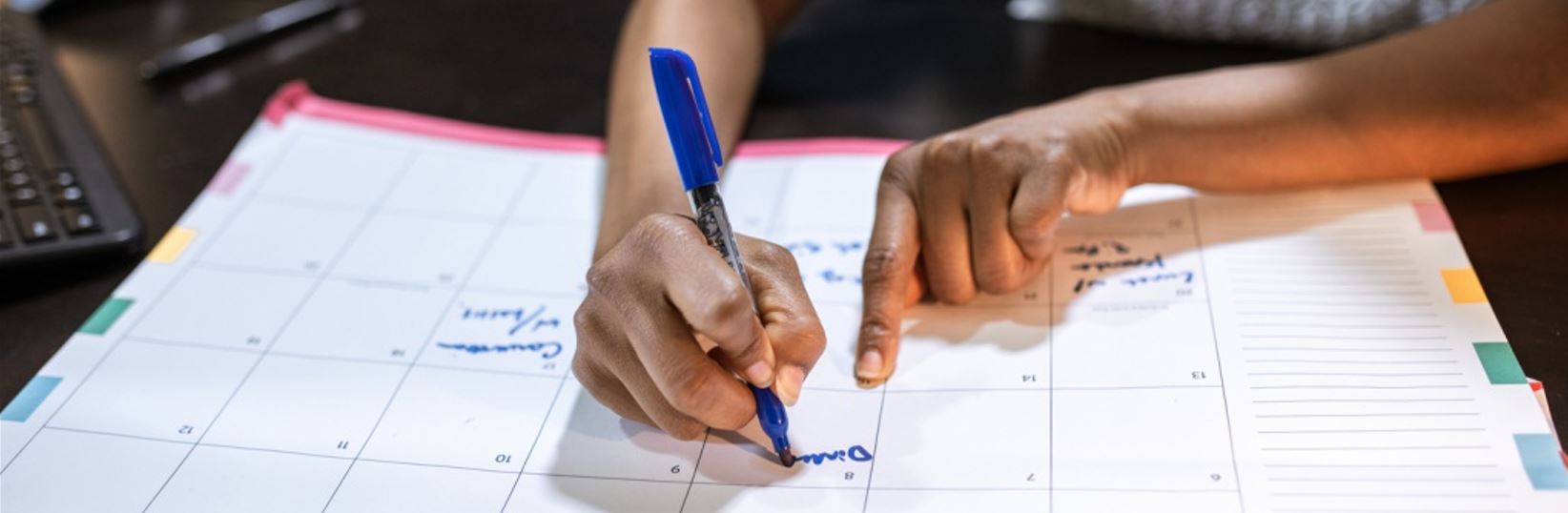 Women writing with blue marker on a desk calendar.