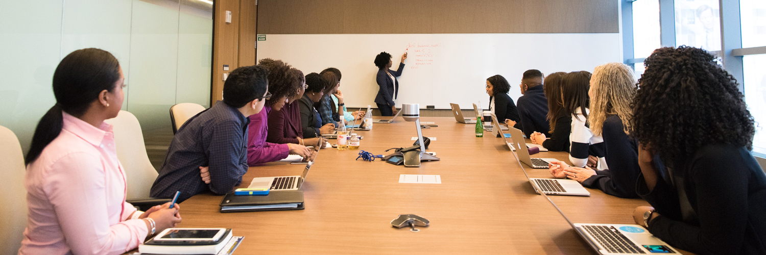 employees sitting around the table while presenter stands at the board