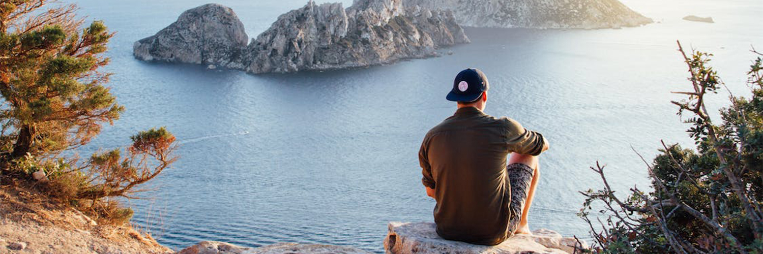Man sitting on cliff overlooking the water