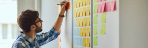 Young creative man writing down ideas on wall full of sticky notes